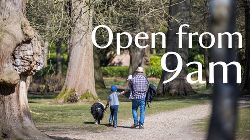 A man with babe in arms and a dog with a little boy between both. He is holding a dog's lead in one hand and the child's hand in the other. Their backs are facing the camera walking along the pathway at Claremont Landscape Garden. There is graphic text over the top that reads 'Open from 9am'.